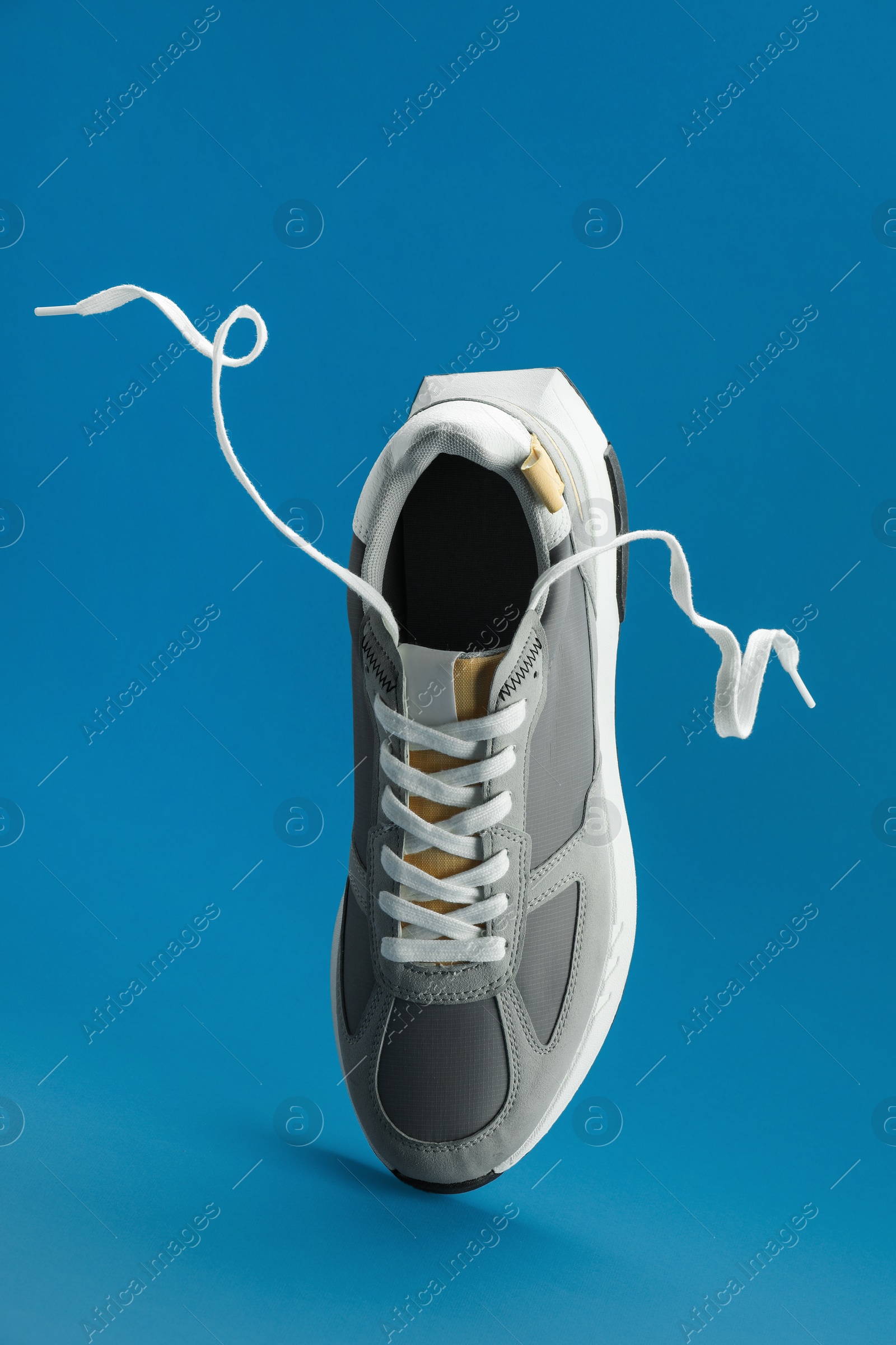 Photo of One stylish grey sneaker levitating on blue background