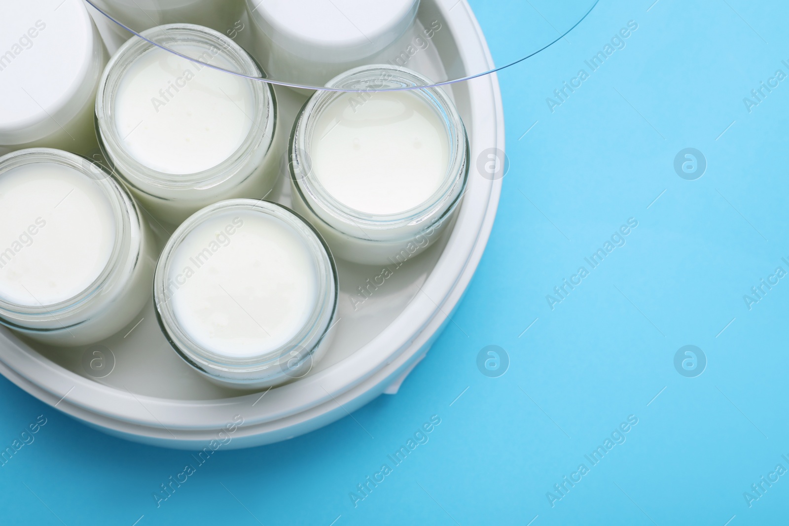 Photo of Modern yogurt maker with full jars on light blue background, top view. Space for text