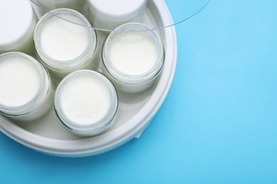 Modern yogurt maker with full jars on light blue background, top view. Space for text