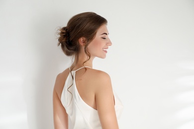 Young bride wearing beautiful wedding dress on light background