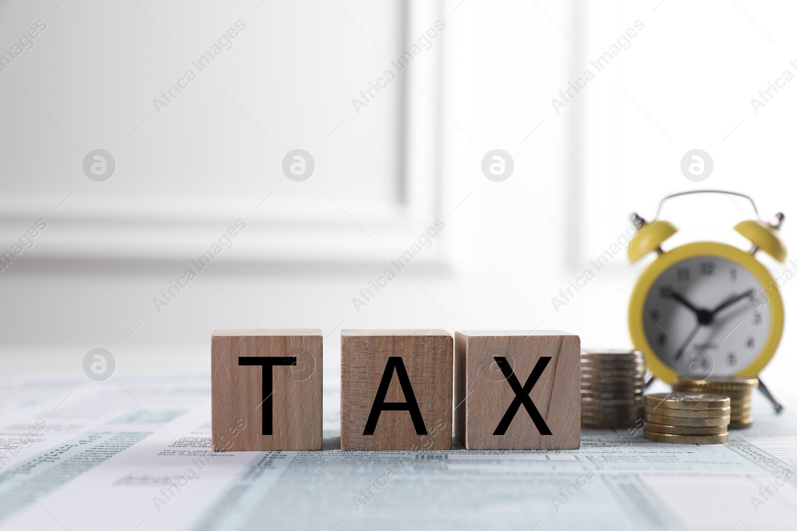 Photo of Wooden cubes with word Tax, coins and alarm clock on document against light background, space for text