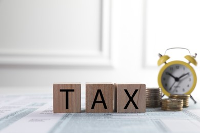 Wooden cubes with word Tax, coins and alarm clock on document against light background, space for text