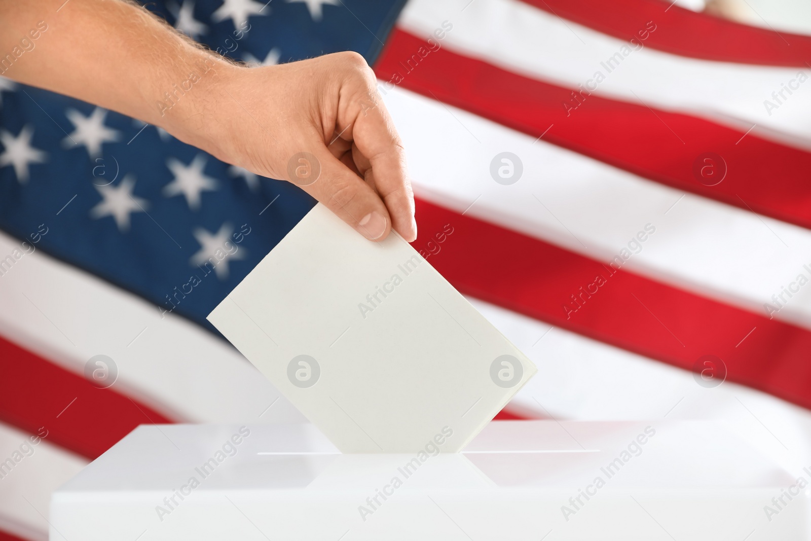 Photo of Man putting ballot paper into box and American flag on background, closeup