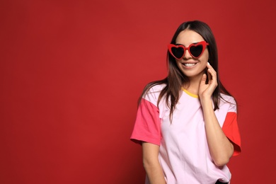 Photo of Portrait of beautiful young woman with heart shaped sunglasses on color background. Space for text