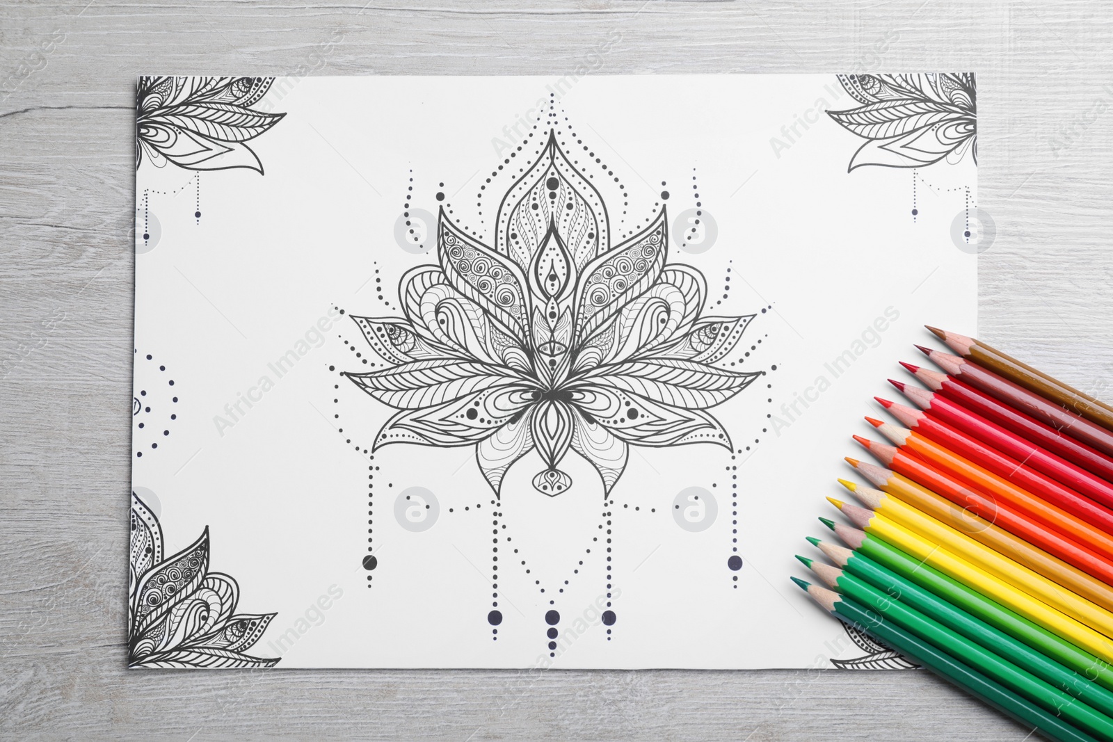 Photo of Antistress coloring page and pencils on light wooden table, flat lay