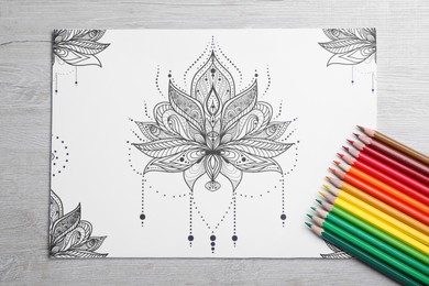 Photo of Antistress coloring page and pencils on light wooden table, flat lay