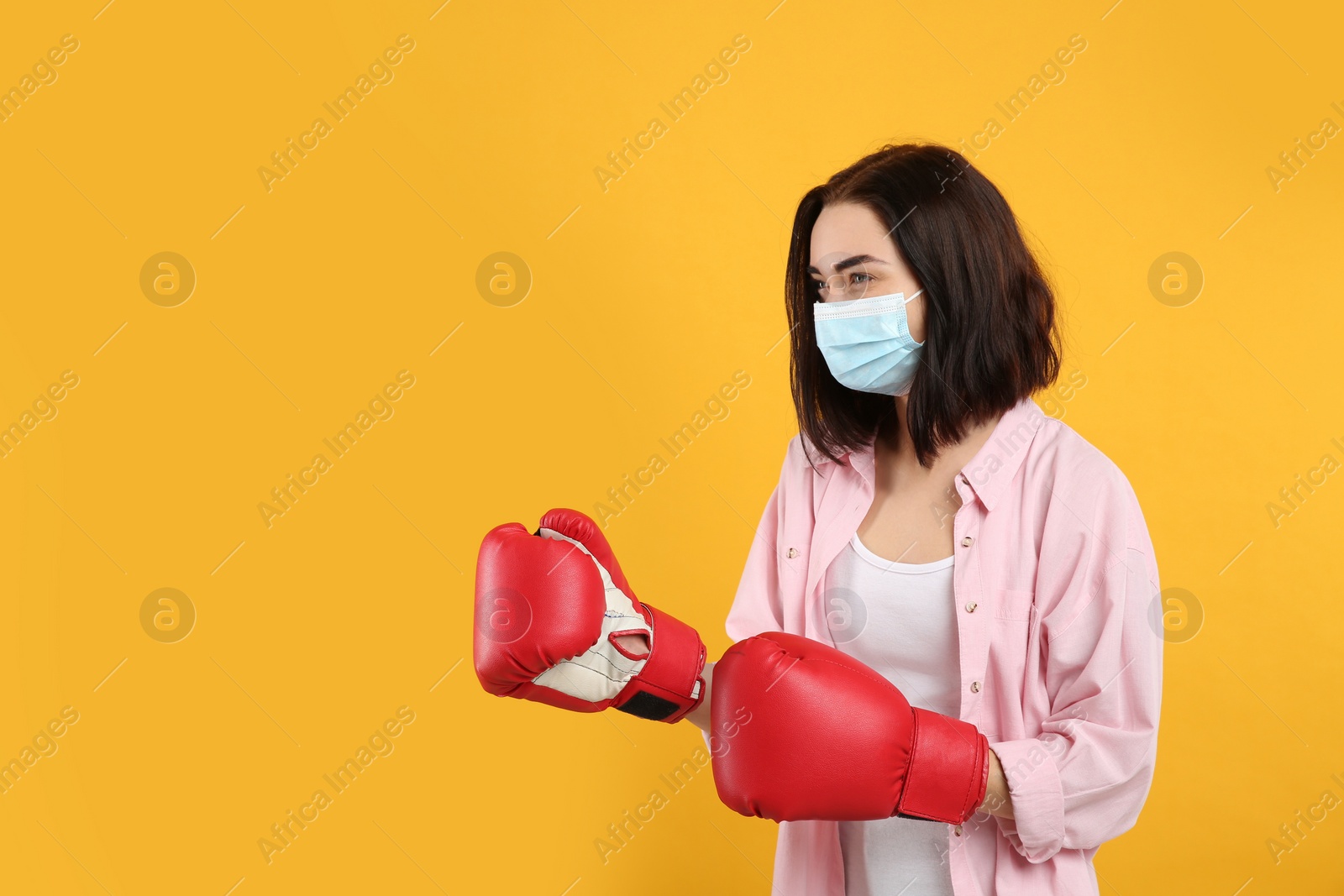 Photo of Woman with protective mask and boxing gloves on yellow background, space for text. Strong immunity concept