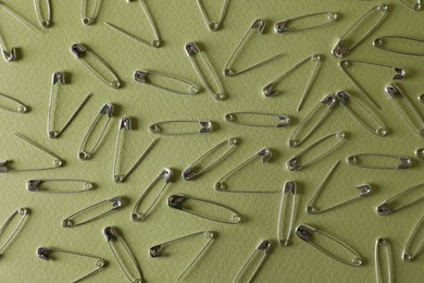 Many safety pins on green background, flat lay