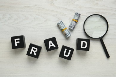 Photo of Black cubes with word Fraud, money and magnifying glass on white wooden table, flat lay