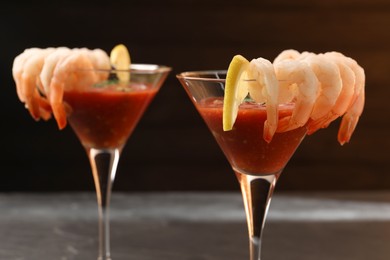 Photo of Tasty shrimp cocktail with sauce in glasses and lemon on grey table, closeup