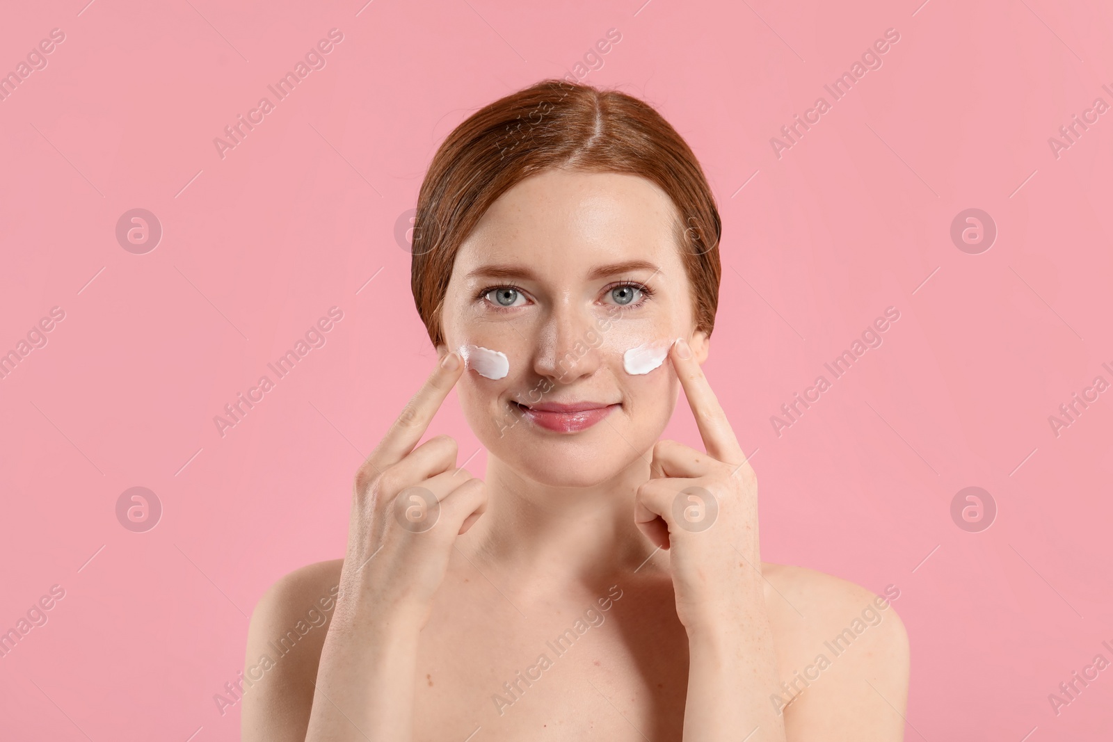 Photo of Beautiful woman with freckles and cream on her face against pink background