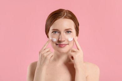 Photo of Beautiful woman with freckles and cream on her face against pink background