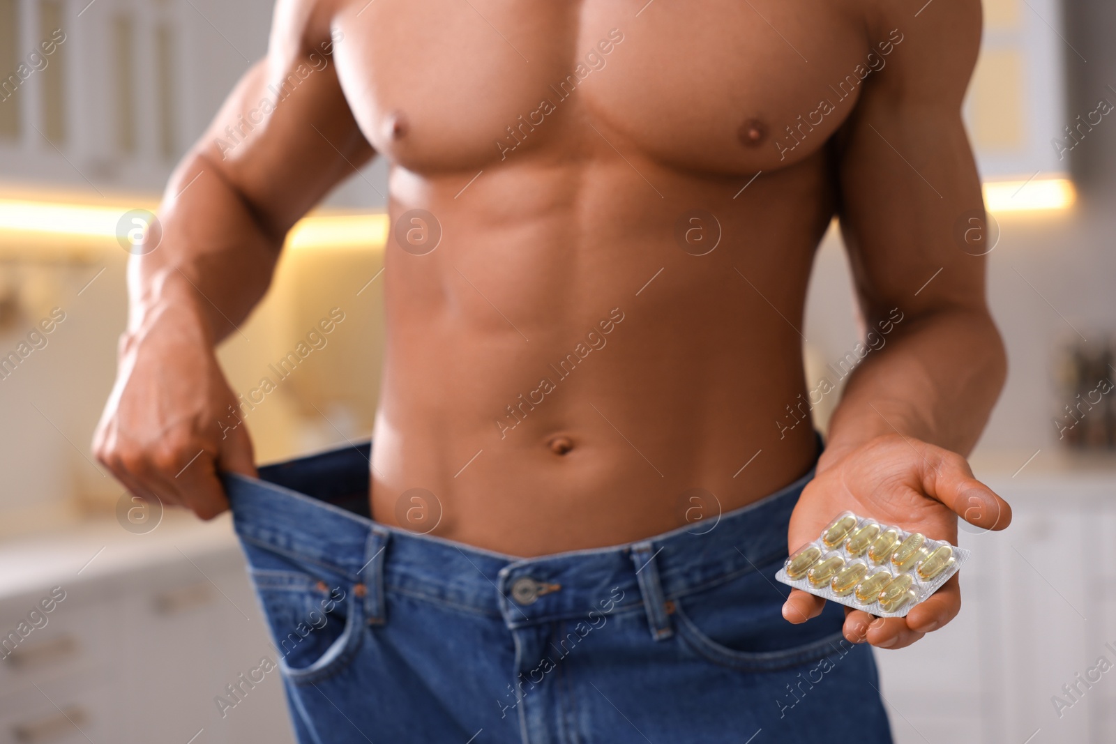 Photo of Athletic man with pills wearing big jeans indoors, closeup. Weight loss