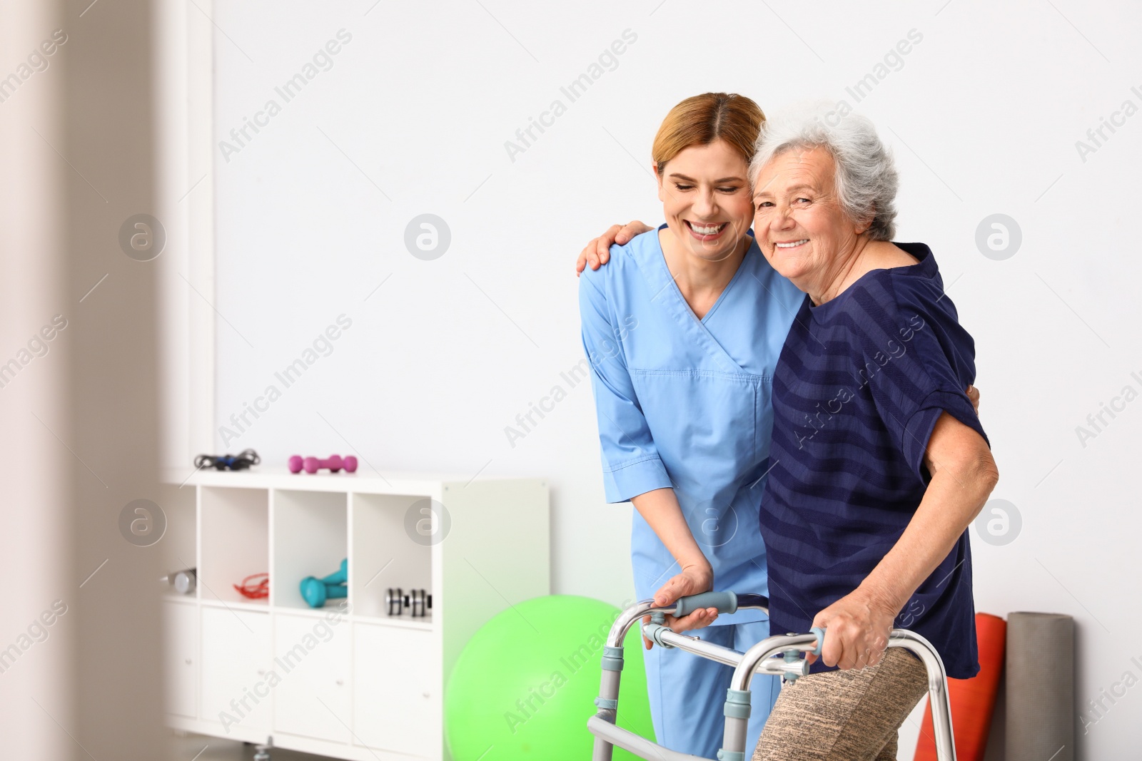 Photo of Caretaker helping elderly woman with walking frame indoors