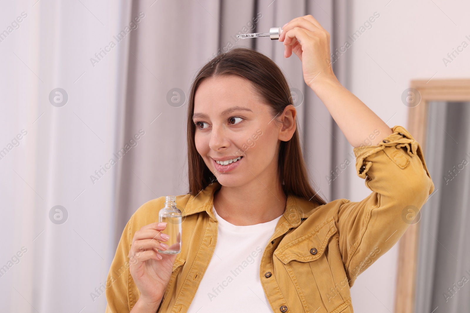 Photo of Beautiful woman applying serum onto hair indoors