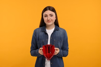 Photo of Sad woman showing empty wallet on orange background