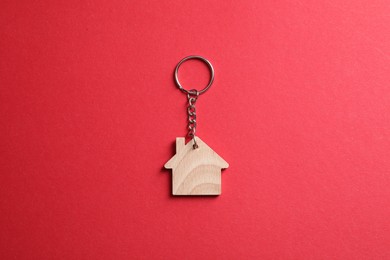 Photo of Wooden keychain in shape of house on red background, top view