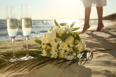 Photo of Beautiful wedding bouquet, glasses of champagne and bride on sandy beach