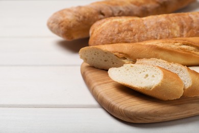 Photo of Cut tasty baguette on white wooden table. Space for text