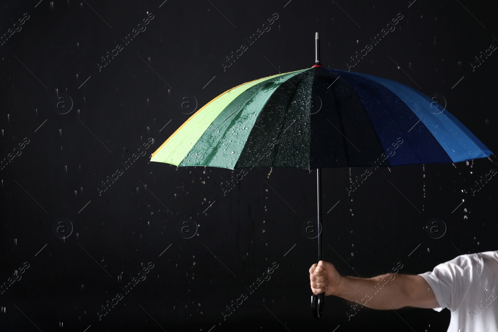 Photo of Man holding color umbrella under rain against black background, closeup