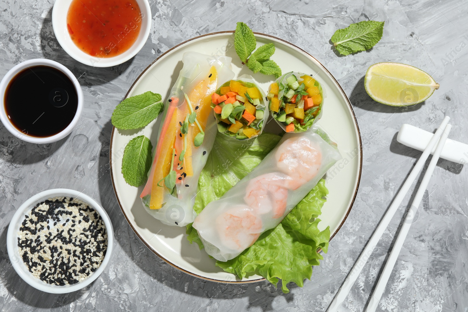 Photo of Tasty spring rolls served on grey textured table, flat lay