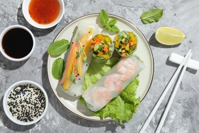 Photo of Tasty spring rolls served on grey textured table, flat lay