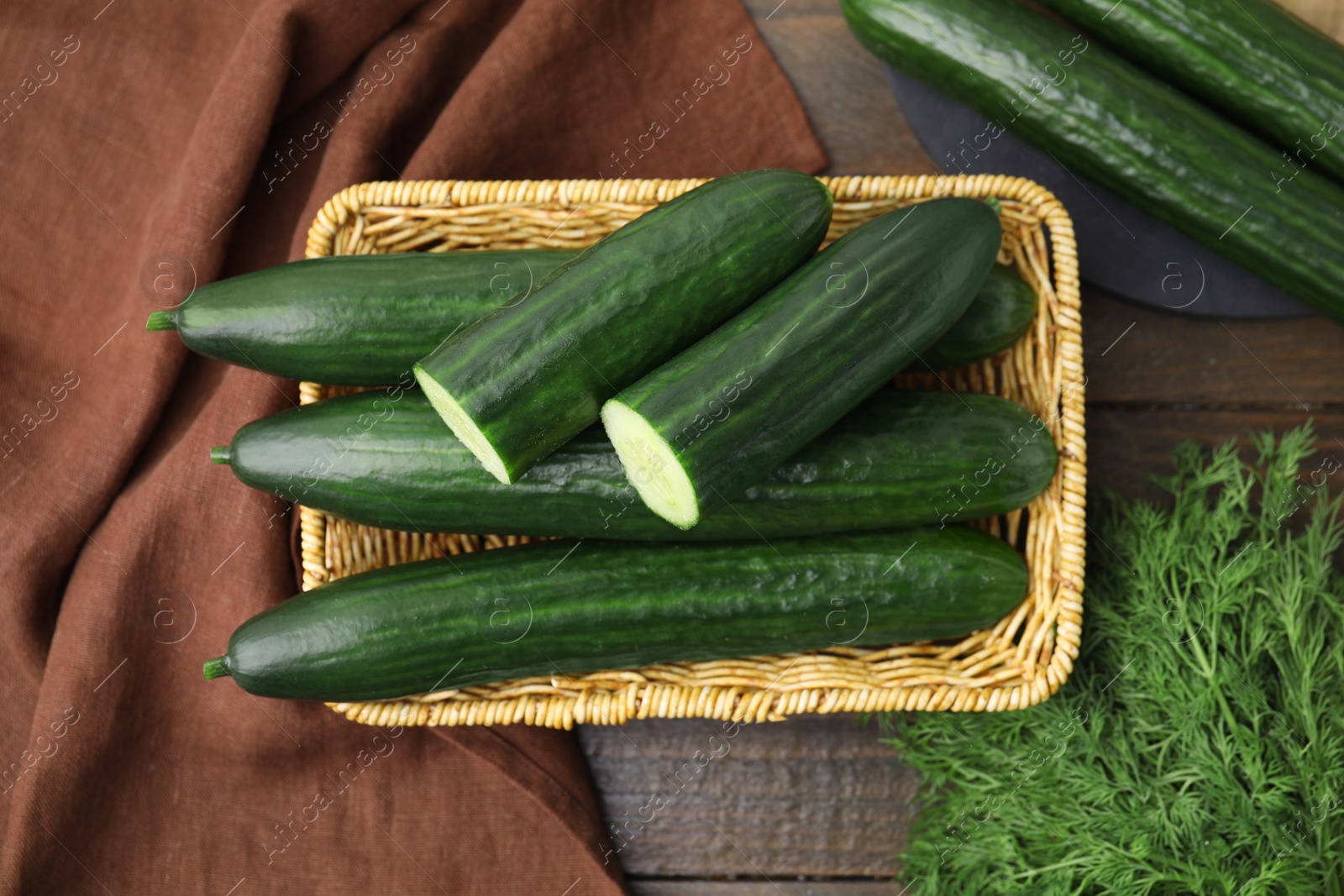 Photo of Fresh cucumbers in wicker basket and dill on wooden table, flat lay