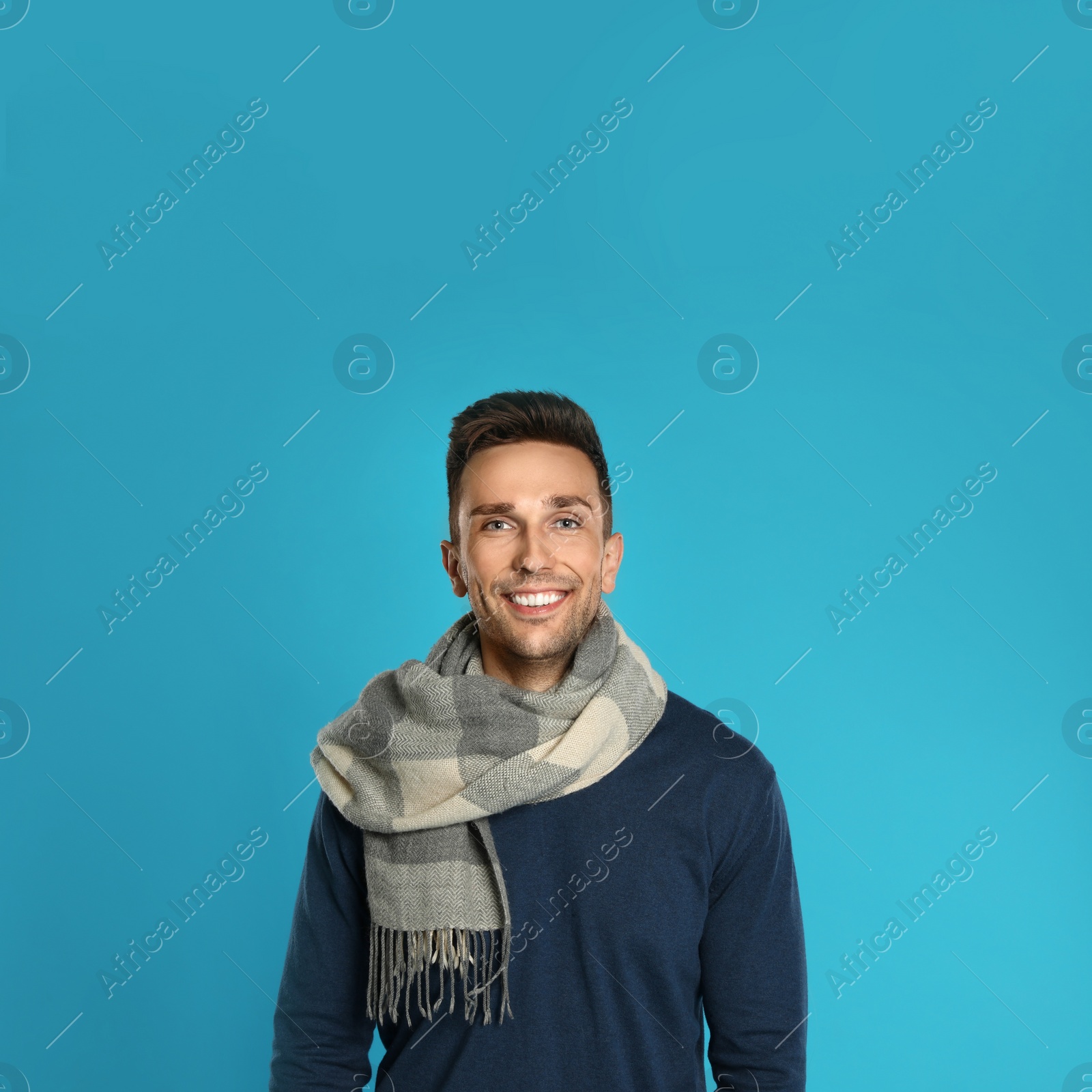 Photo of Happy young man in scarf and warm sweatshirt on blue background. Winter season