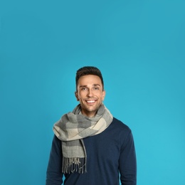 Happy young man in scarf and warm sweatshirt on blue background. Winter season