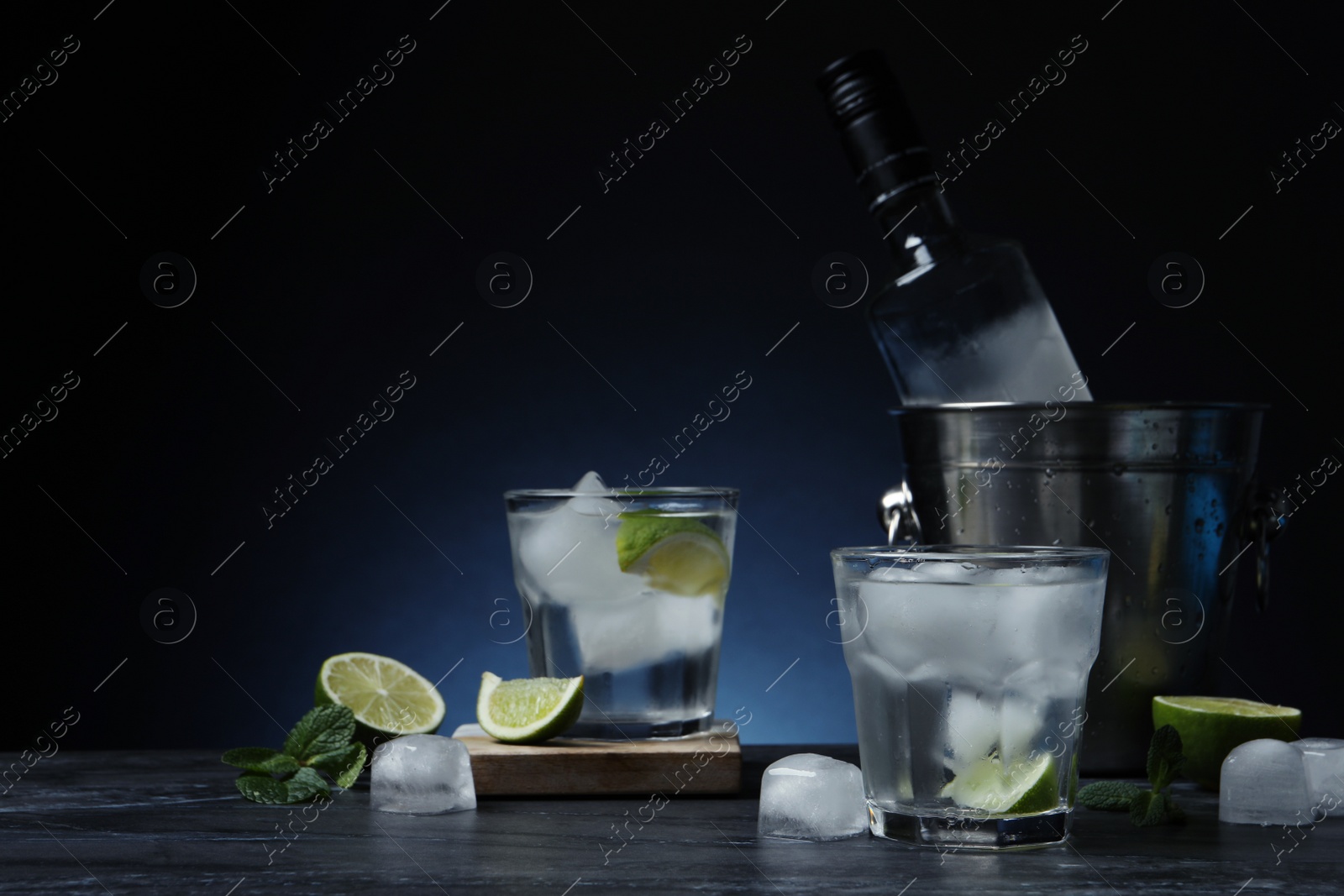 Photo of Bottle of vodka, glasses, lime, mint and ice on black marble table. Space for text