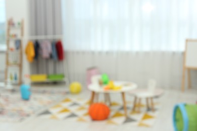 Photo of Blurred view of child`s playroom with different toys and furniture. Stylish kindergarten interior