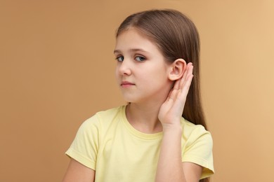 Little girl with hearing problem on pale brown background