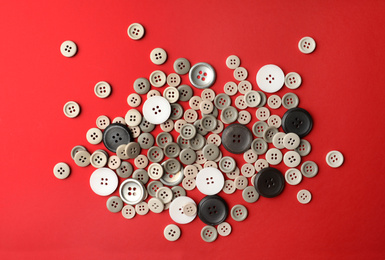 Many colorful sewing buttons on red background, flat lay