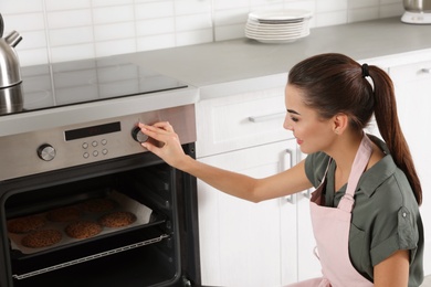 Photo of Young woman baking cookies in oven at home