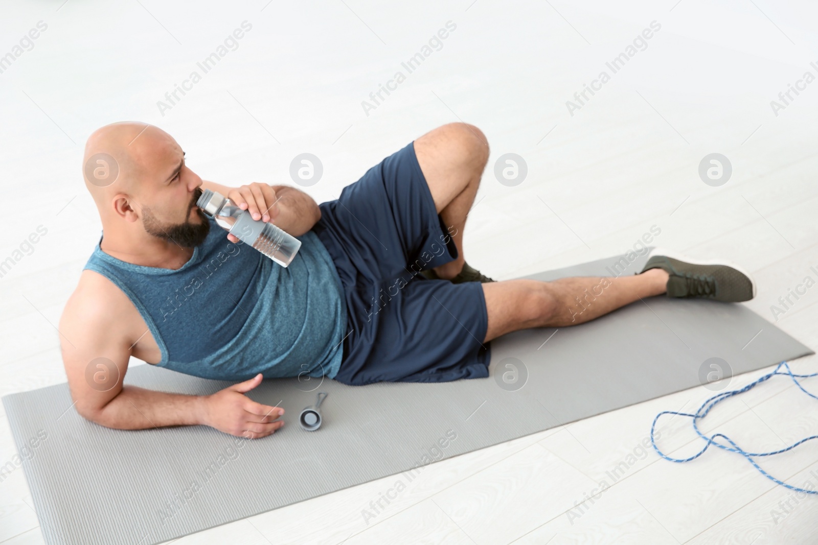 Photo of Tired overweight man drinking water in gym