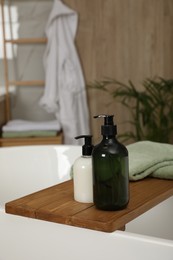 Wooden bath tray with bottles of shower gels and towel on tub indoors, space for text