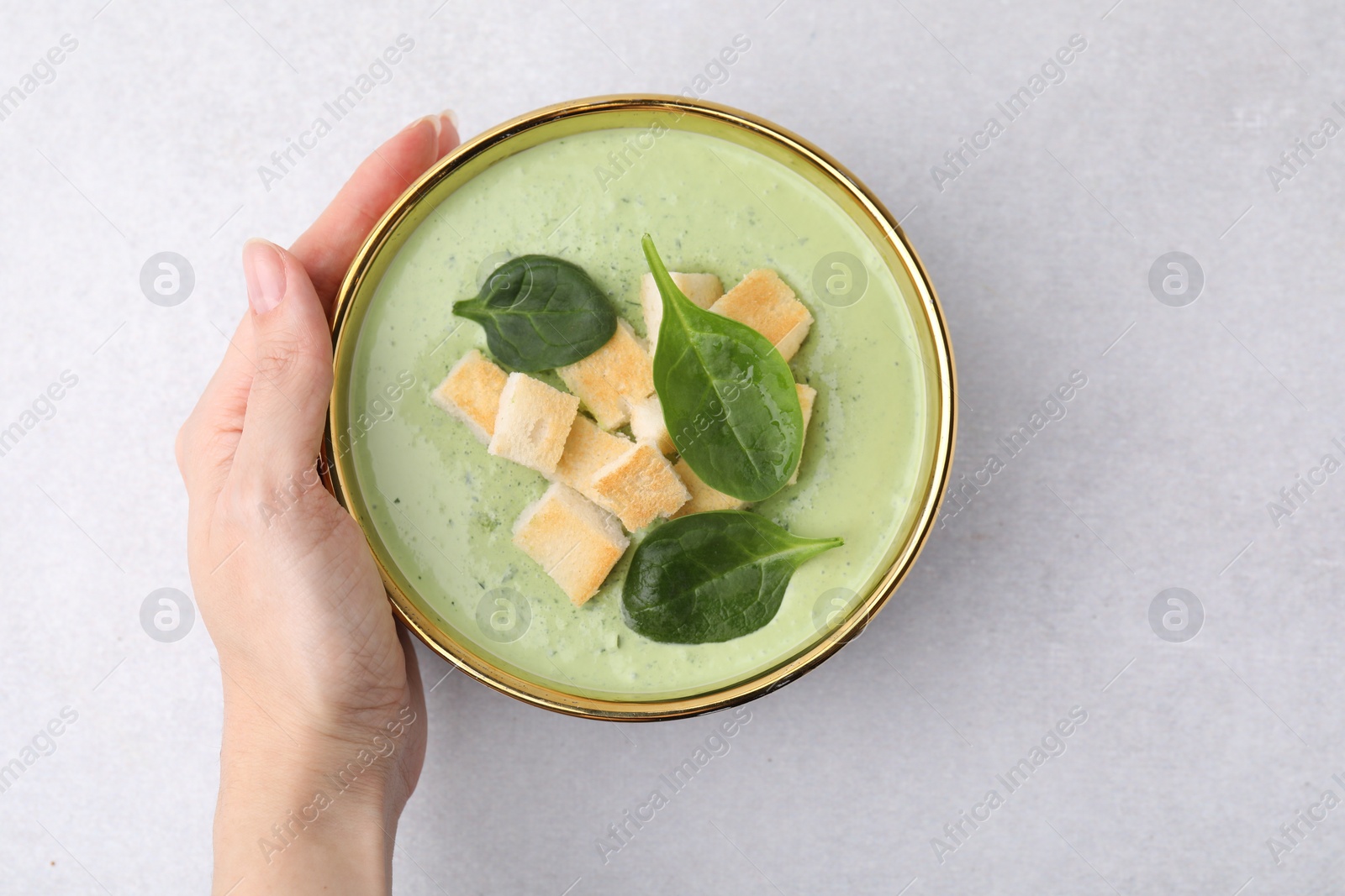 Photo of Woman with bowl of delicious spinach cream soup on light grey table, top view