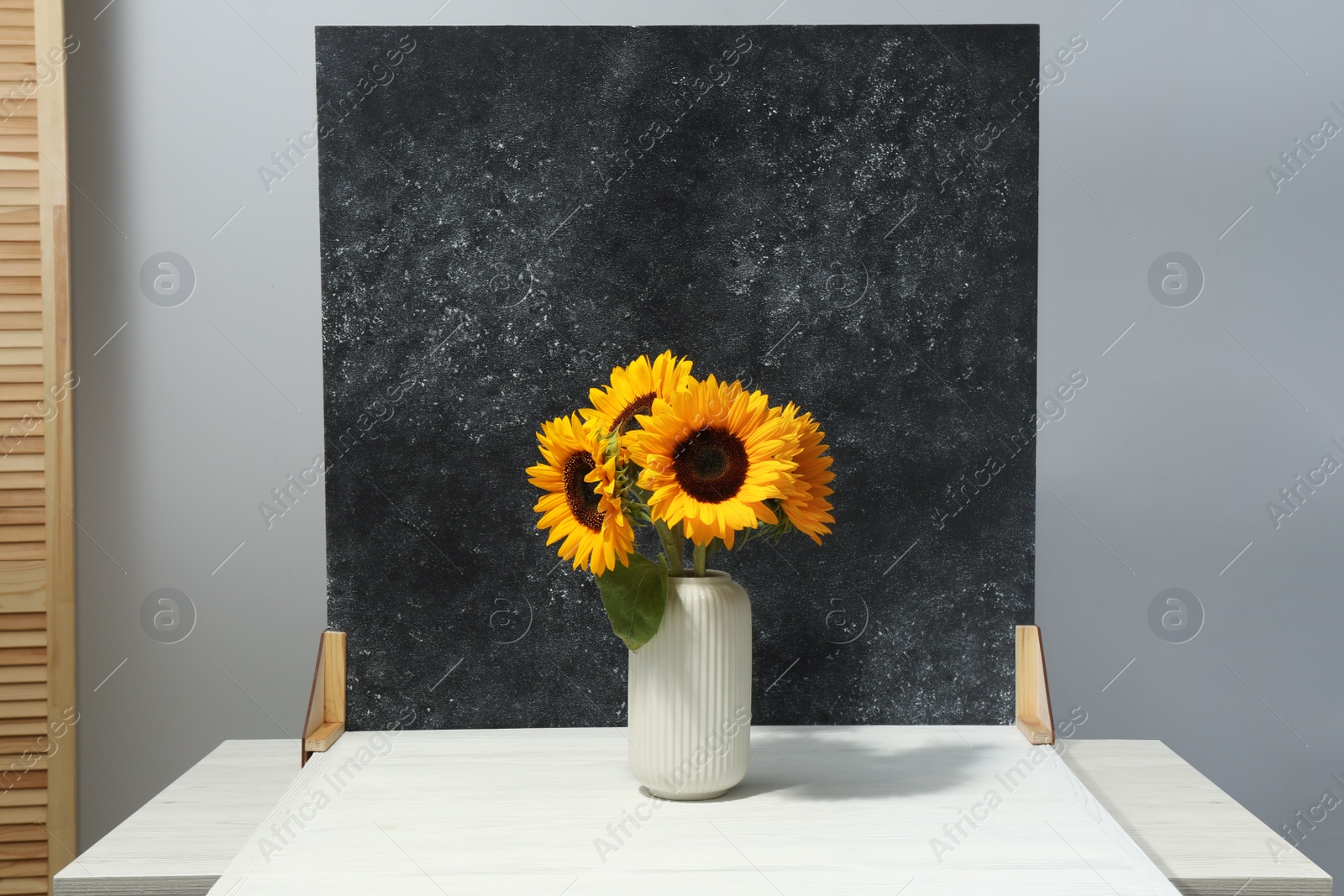 Photo of Vase with beautiful sunflowers and double-sided backdrop on table in photo studio