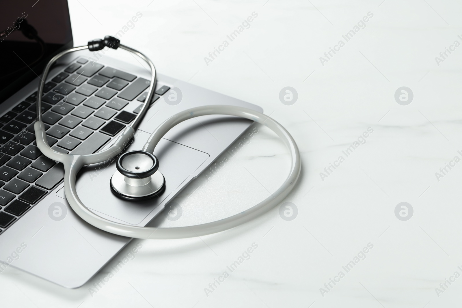 Photo of Modern laptop and stethoscope on white table. Space for text