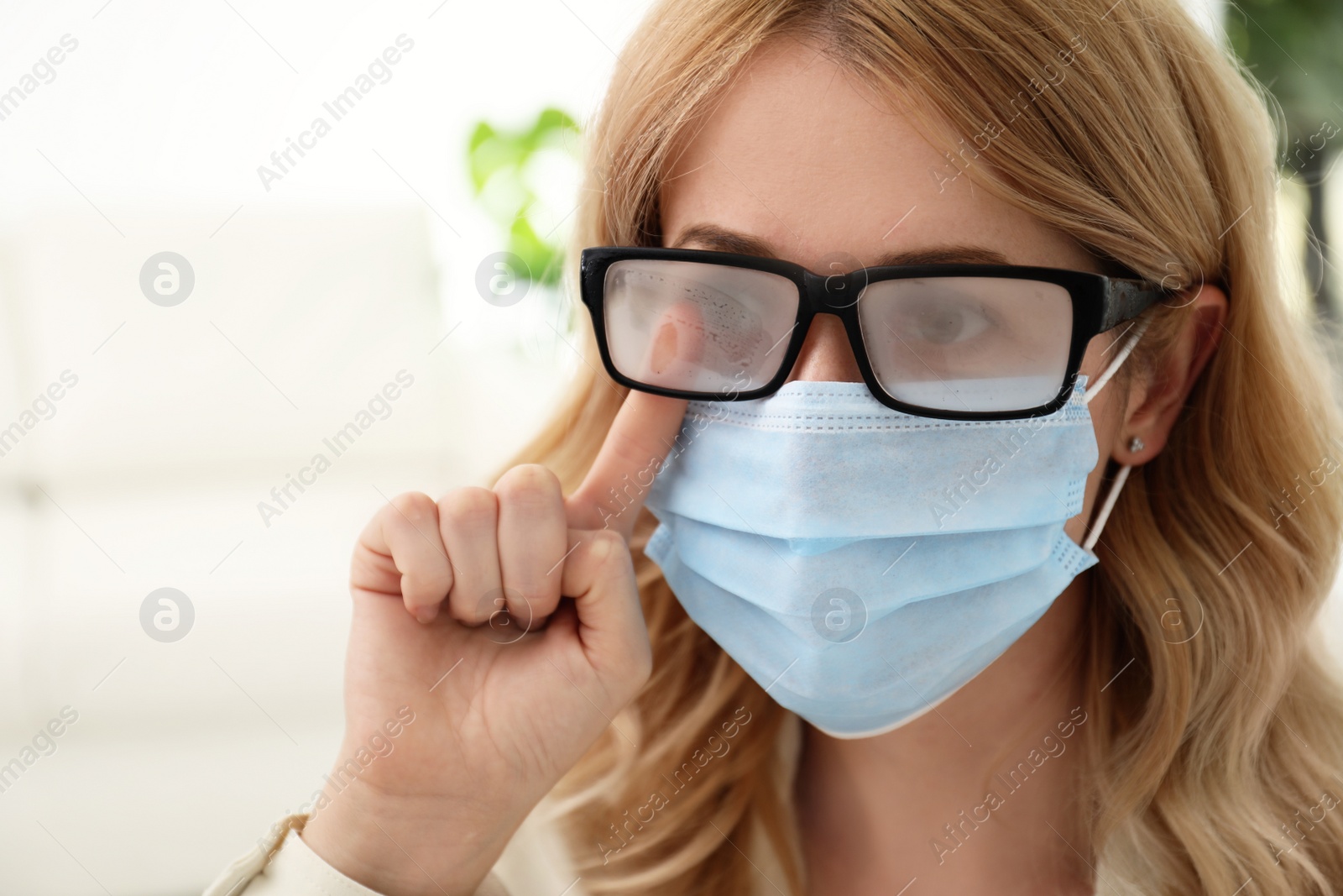 Photo of Woman wiping foggy glasses caused by wearing medical mask indoors, closeup