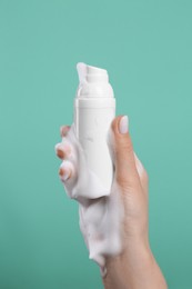 Photo of Woman with foam on hand holding bottle of skin cleanser against green background, closeup. Cosmetic product