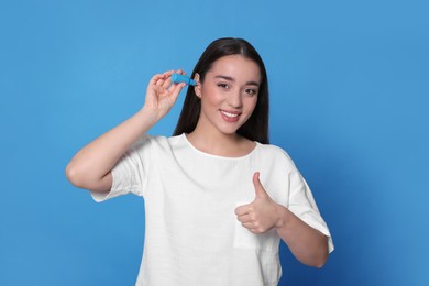 Young woman using ear drops on light blue background