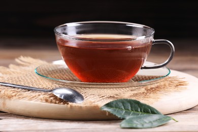 Photo of Aromatic hot tea in glass cup and leaves on wooden table, closeup