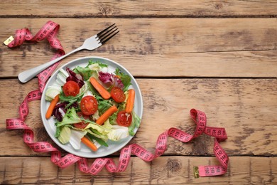 Photo of Plate of fresh vegetable salad, fork and measuring tape on wooden table, flat lay with space for text. Healthy diet concept