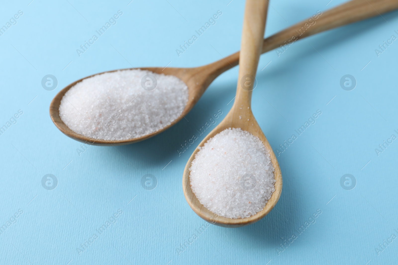 Photo of Organic white salt in spoons on light blue background, closeup