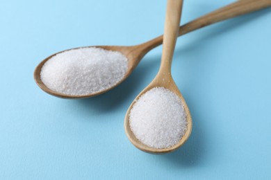 Organic white salt in spoons on light blue background, closeup