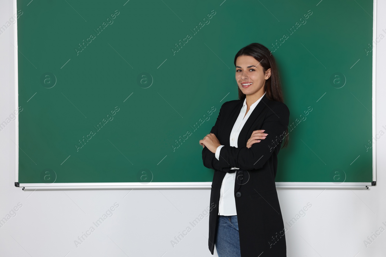 Photo of Happy young teacher giving lesson at blackboard in classroom. Space for text