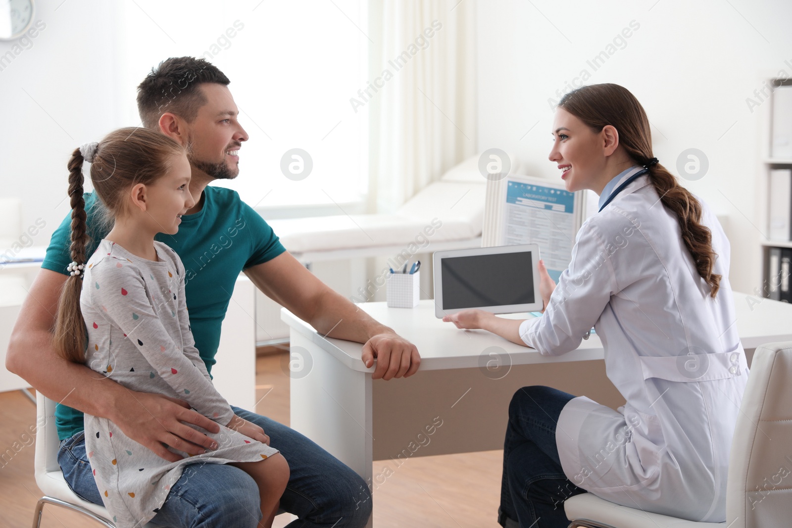 Photo of Father and daughter visiting pediatrician. Doctor working with little patient in hospital