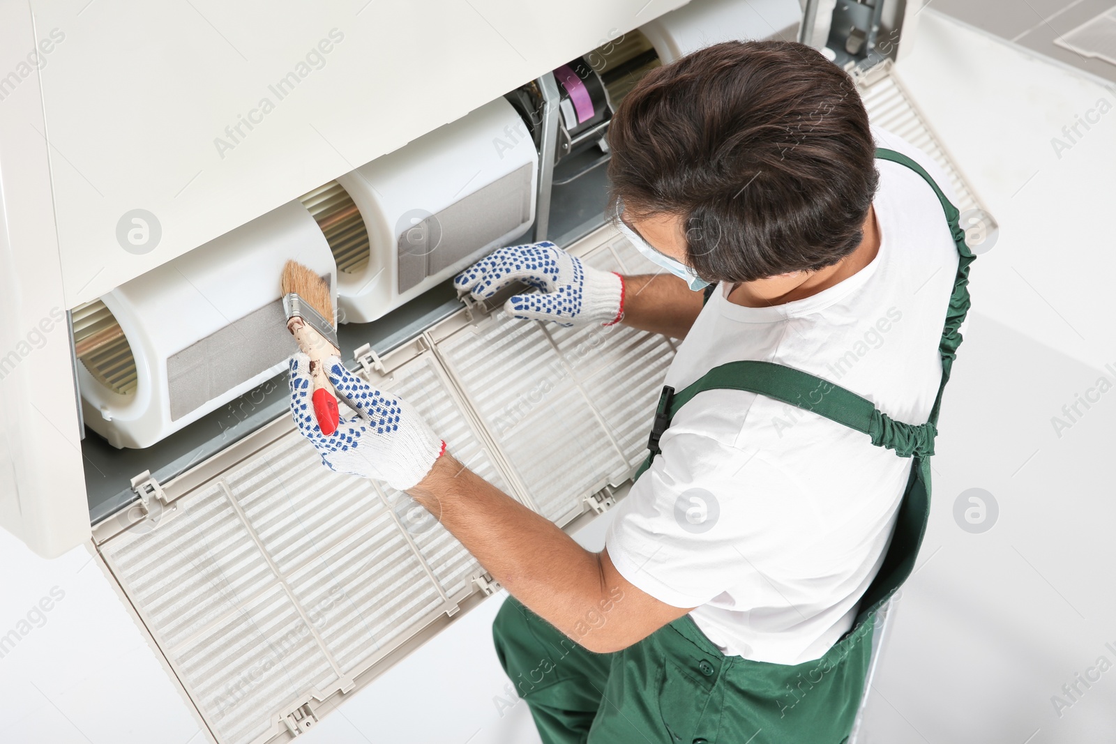 Photo of Young male technician cleaning air conditioner indoors