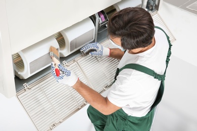 Photo of Young male technician cleaning air conditioner indoors